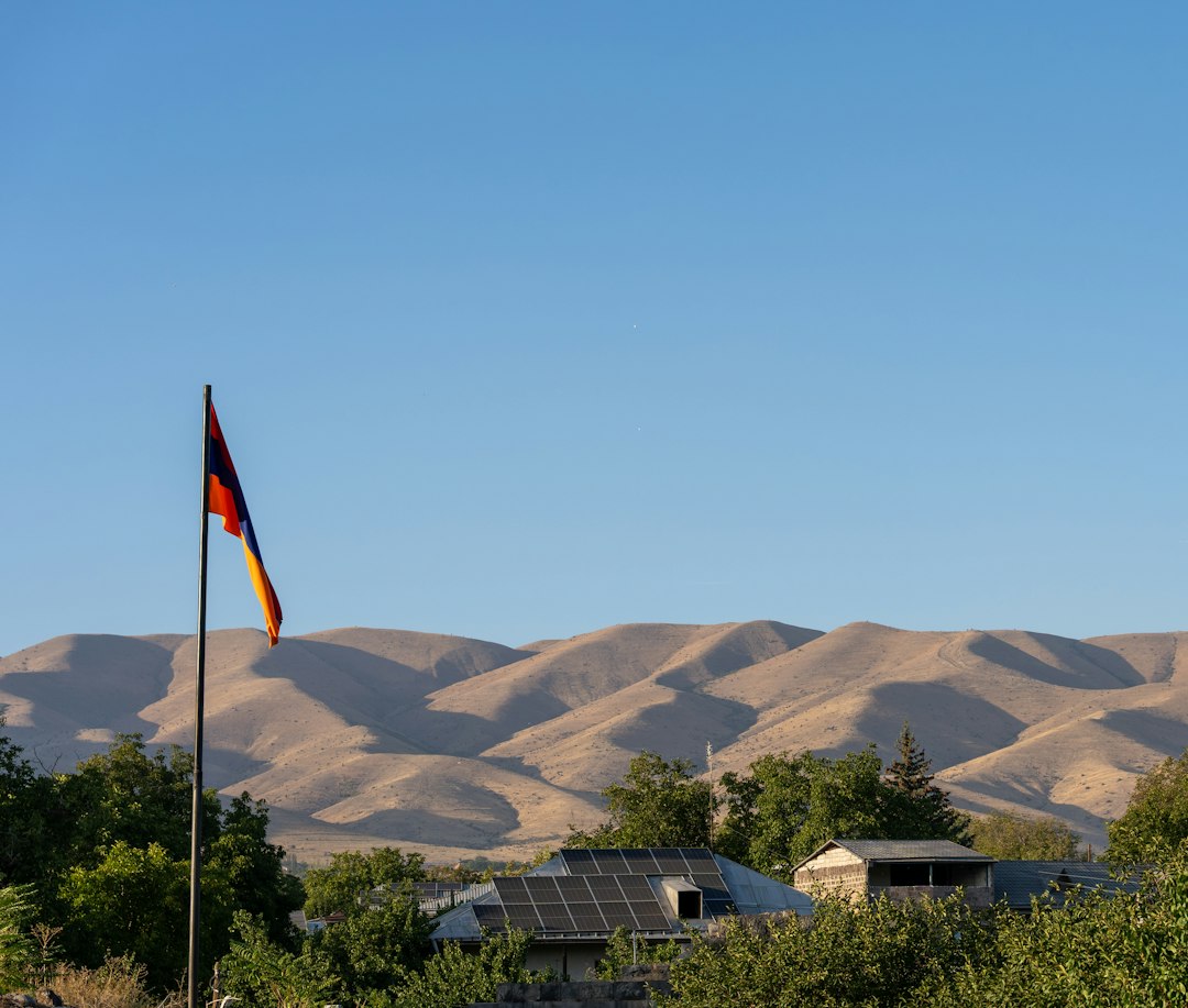 Estructuras de Fijación para Placas Solares: Tejado de Teja, Chapa y Plana: The flag of Armenia flying on a pole above houses with solar panels before rolli