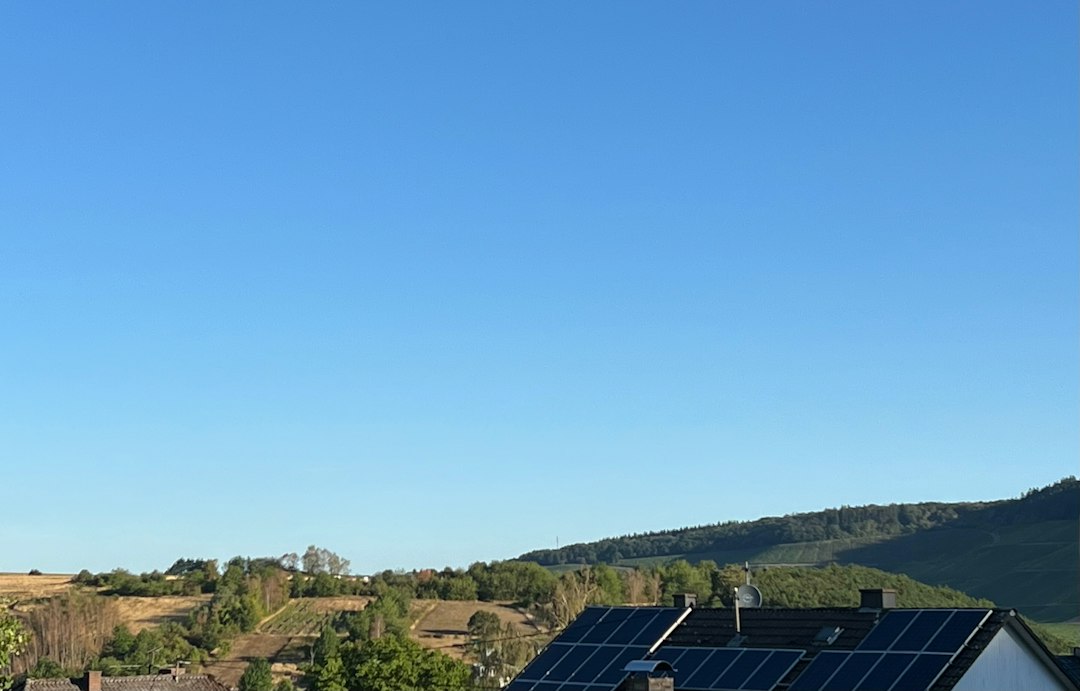 Orientación e Inclinación Óptima de Placas Solares Según la Latitud en España: Solar panels on a roof overlooking a green hillside under a clear blue sky